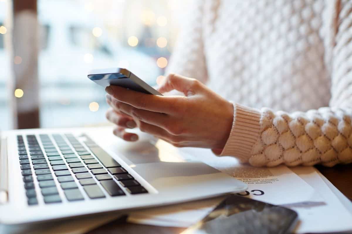 close up of womans hand holding a phone and laptop on a table