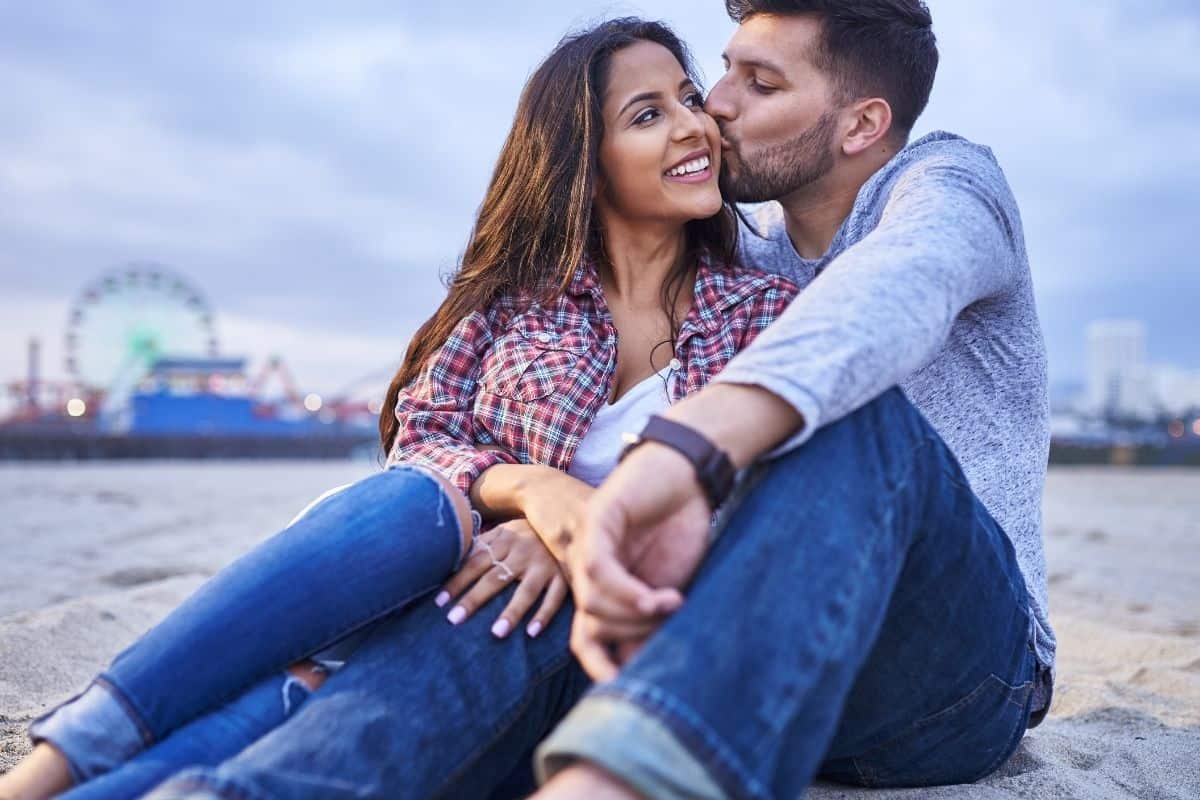 man kissing a woman's cheek outside at the beach