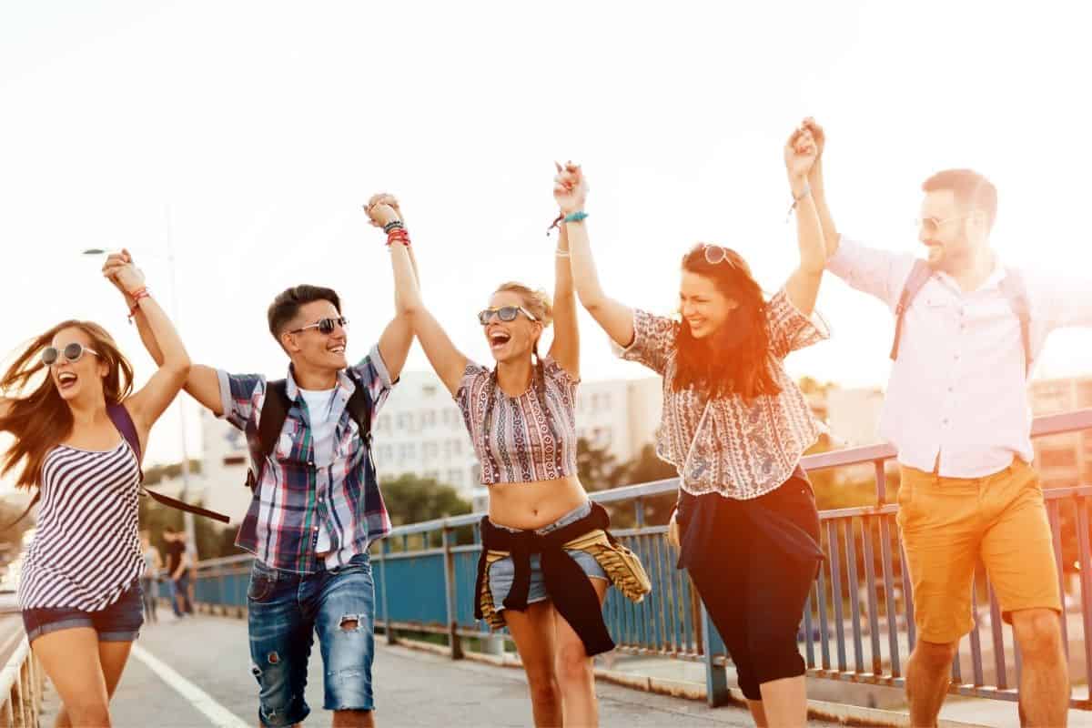 teens outside on a boardwalk walking together hands in the air - happy faces