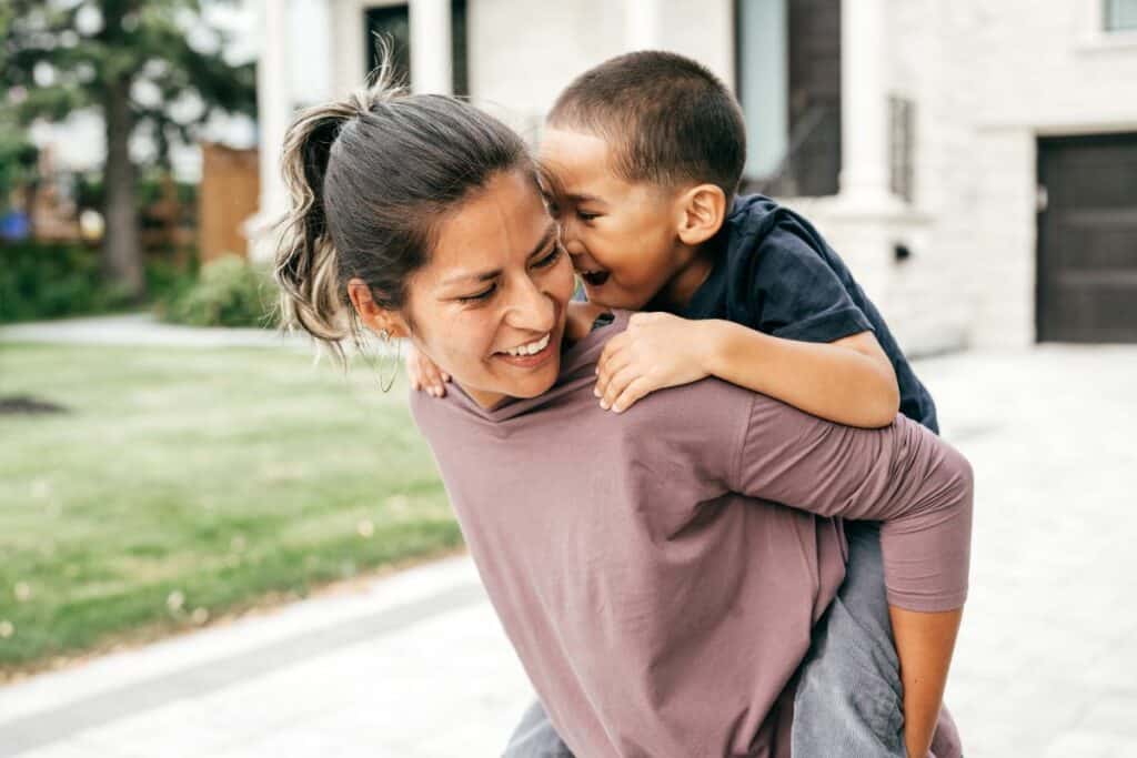 boy mom carrying her son on her back laughing