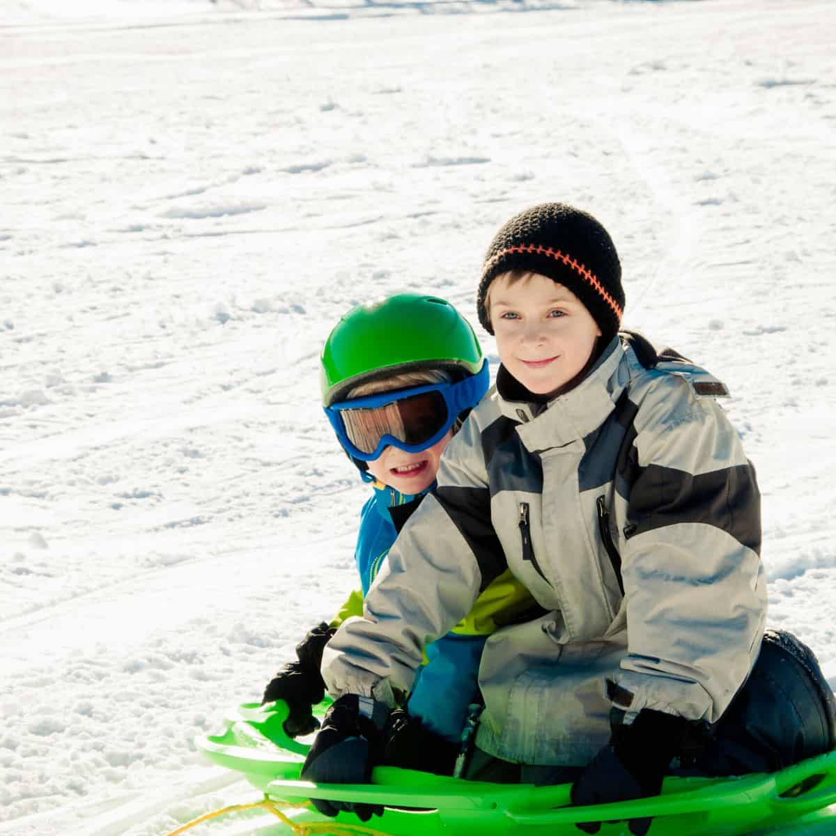 2 kids out in the snow about to sled