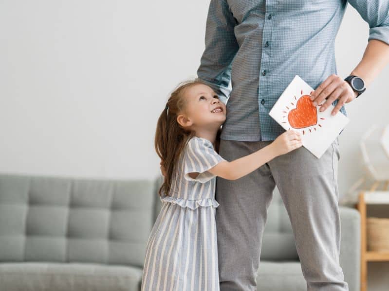 daughter hugging her dad with a homemade card in their hands