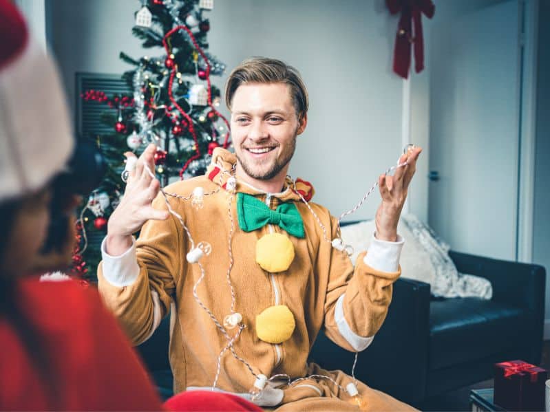 close up of a friend in a gingerbread onesie with twinkle lights around his neck