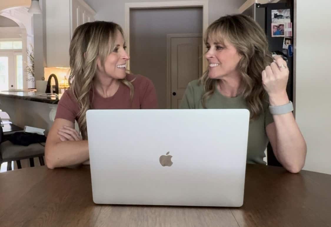 Kim and Kalee at the table looking at each other and their laptop